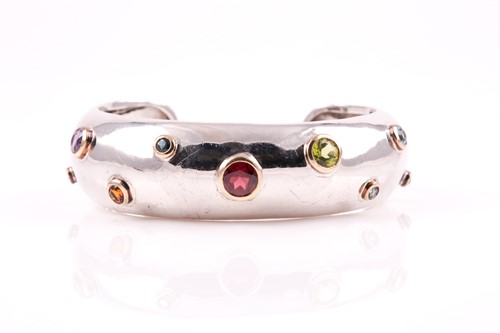 Lot 261 - A multi-gem set bangle, the wide white metal...
