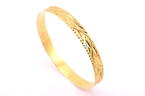 Lot 412 - A yellow metal bangle, with stylised leaves on...