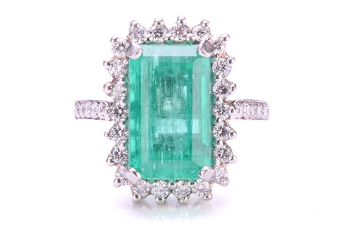 Lot 299 - An emerald and diamond halo ring in platinum,...